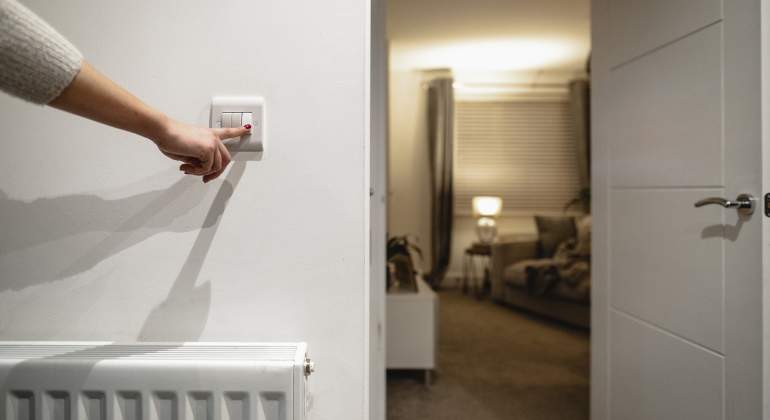 Una mano apaga un interruptor de la luz de una casa cerca de un radiador