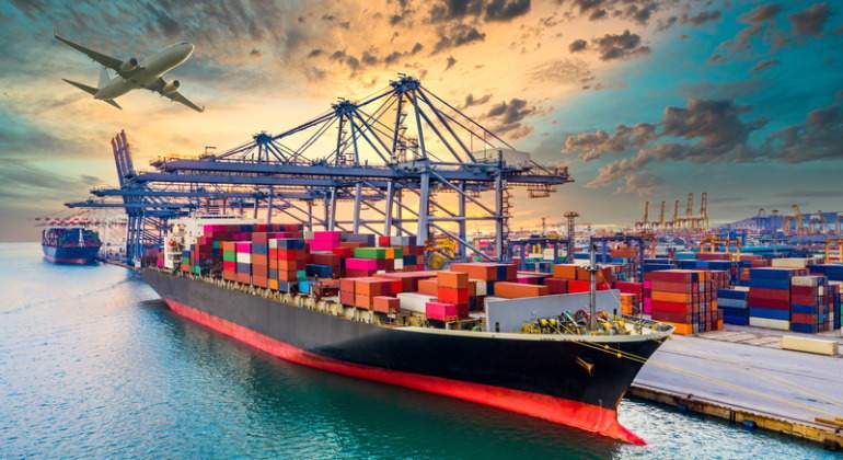 Un barco cargado de mercancas en el puerto con un avin al fondo