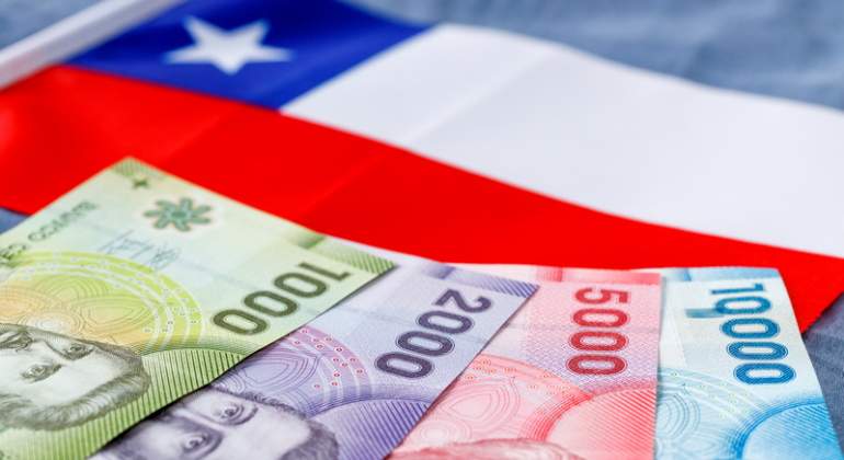 Billetes de pesos chilenos dispuestos en cantidad creciente sobre una bandera de Chile