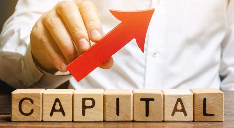 Una mano sostiene una flecha ascendente sobre letras que forman la palabra capital