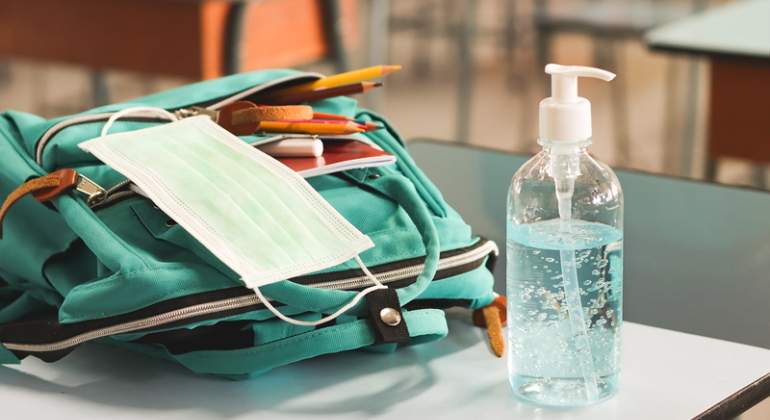 Una mochila una mascarilla y un bote de gel hidroalcohlico encima de un pupitre