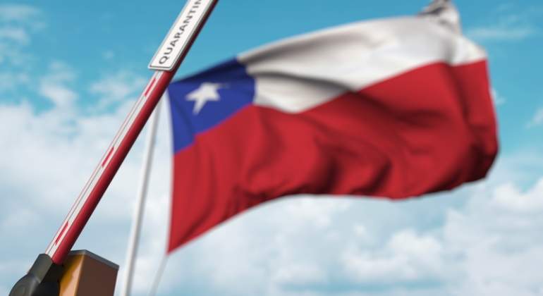 Una barrera con la palabra cuarentena se levanta con la bandera de Chile al fondo