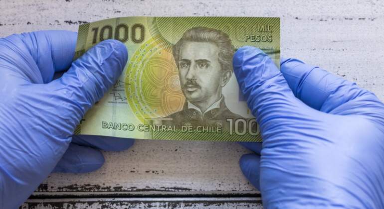 Dos manos con guantes de ltex cogen un billete de mil pesos chilenos
