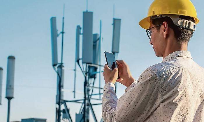 Una persona con casco amarillo sostiene un mvil ante lo que parecen antenas de telefona