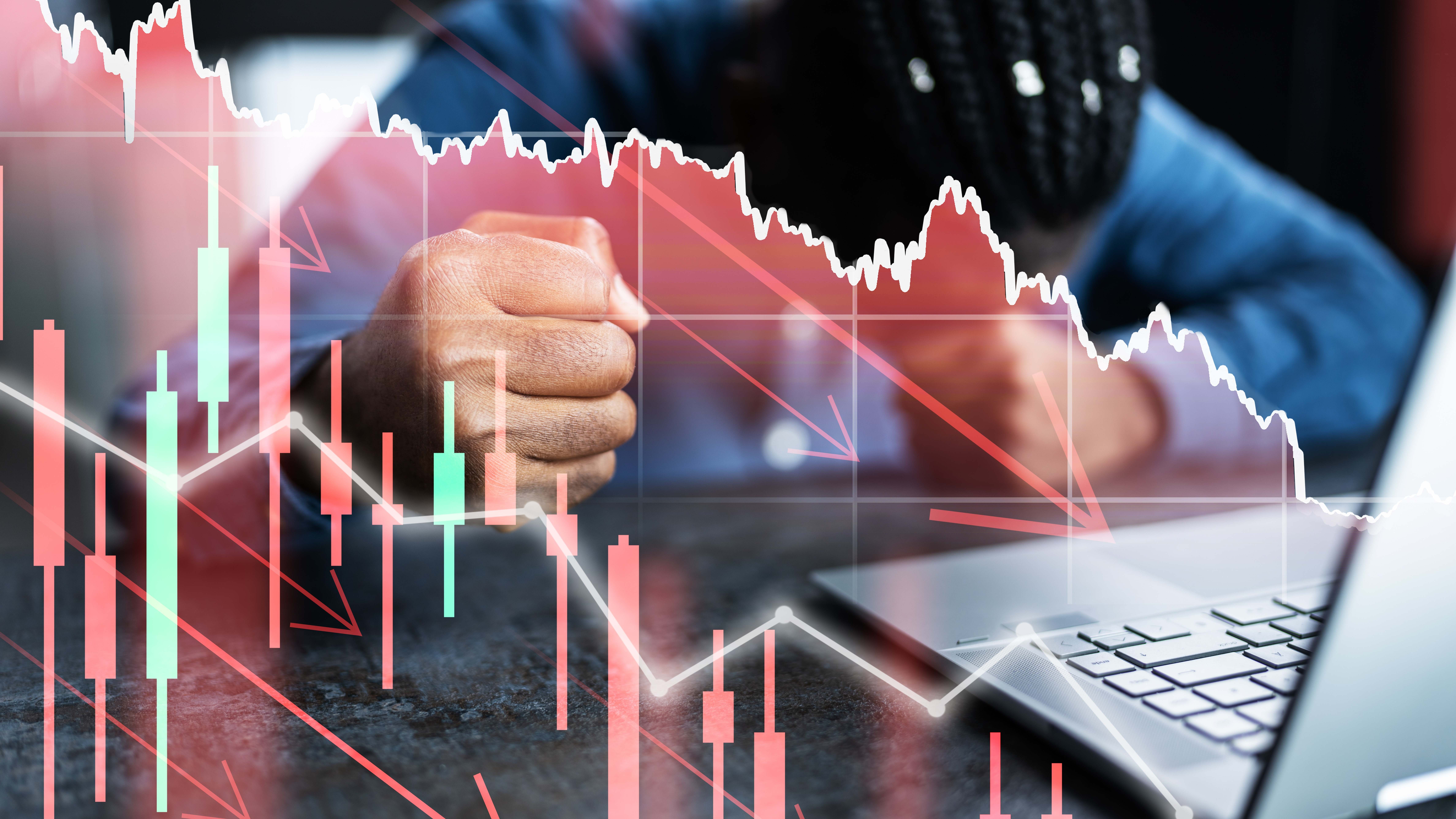 Gráficos de mercado en caída con un inversor que golpea la mesa de fondo