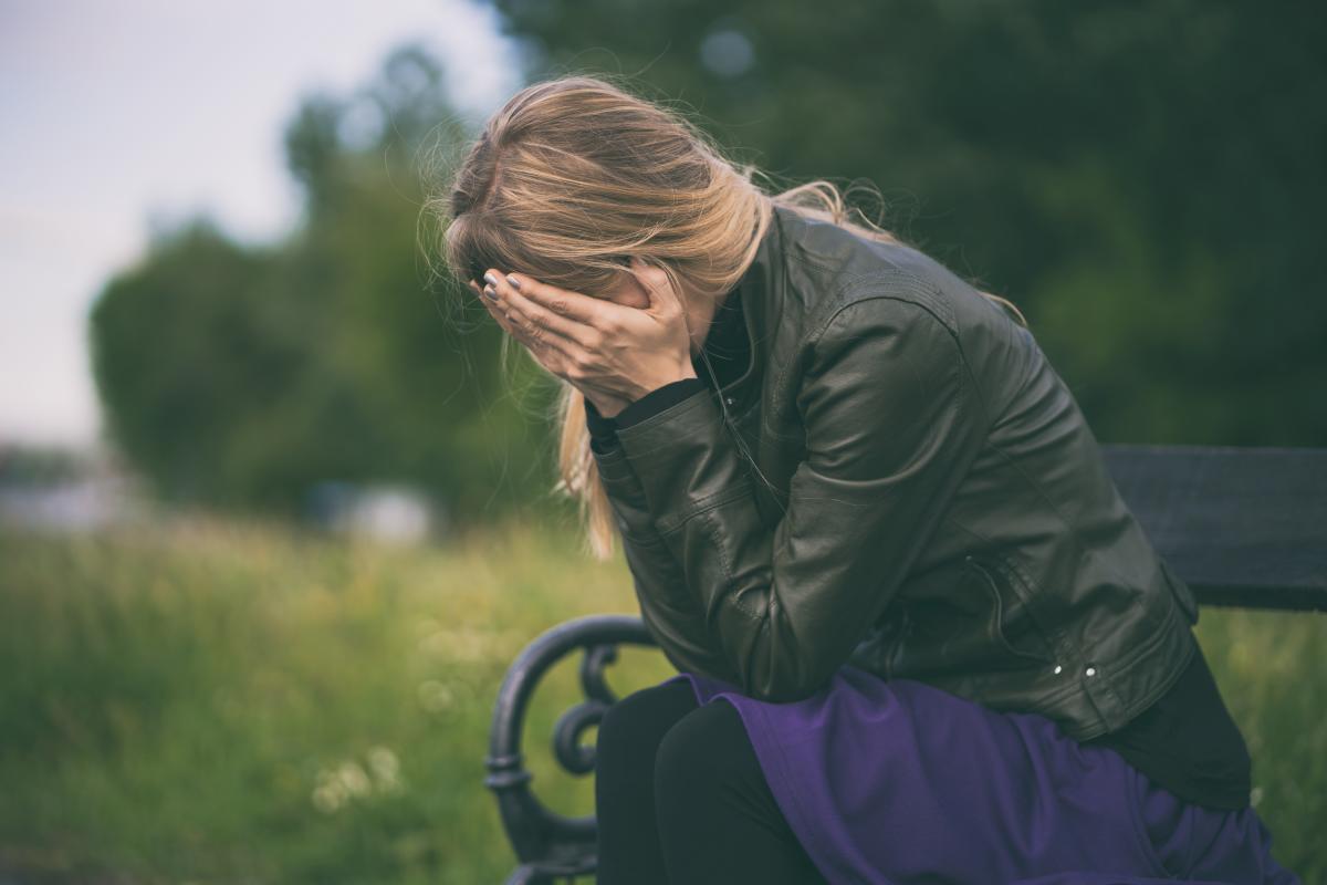 Mujer jóven sentada en un banco se tapa la cara con las manos | Foto de 123rf/djoronimo